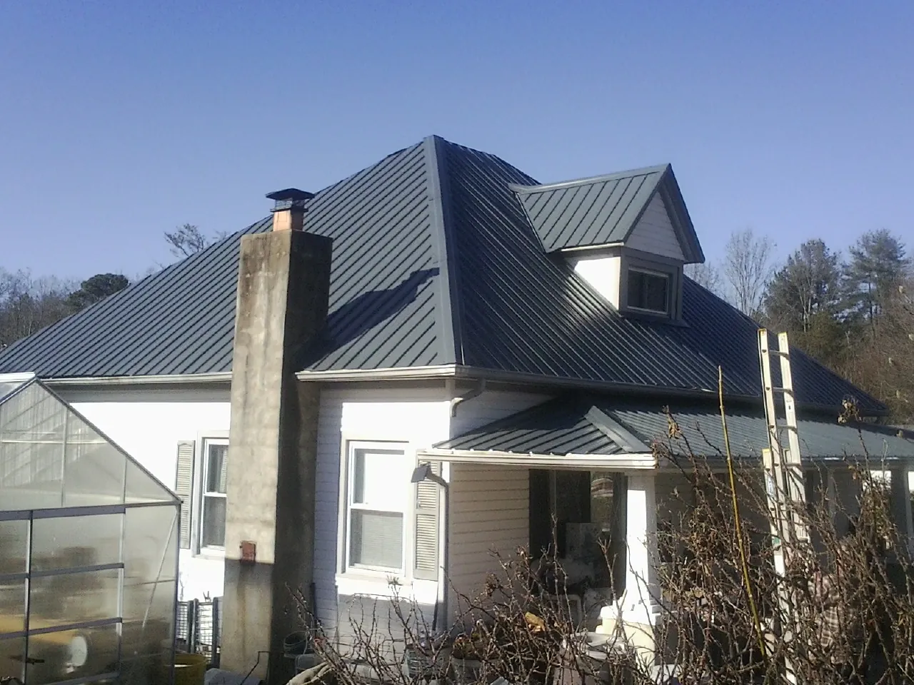 Dark blue standing seam metal roof on a white farmhouse with dormer — Slate & Tile Roof Repair by Roofing Brothers in Andrew