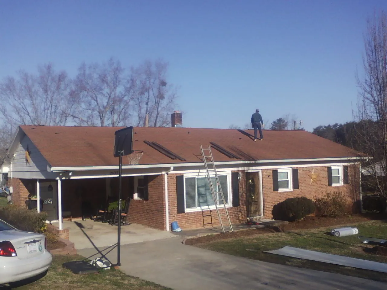 Roofer stripping a shingle roof on a brick ranch before metal panels in Andrew
