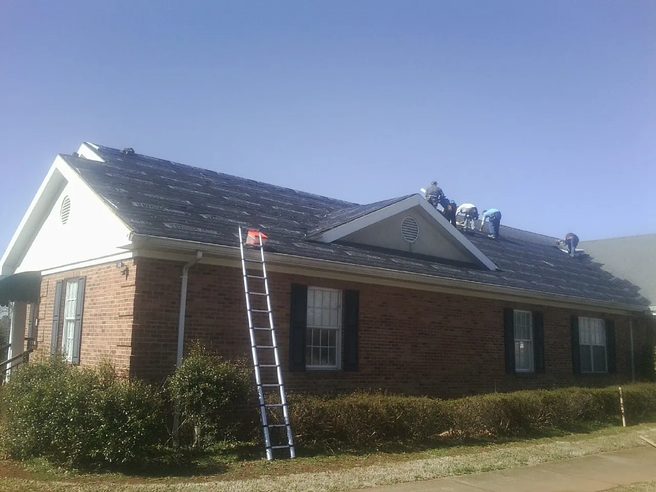 Crew tearing shingles off a brick ranch roof with a ladder set — Emergency Roof Repair work by our crew in Andrew