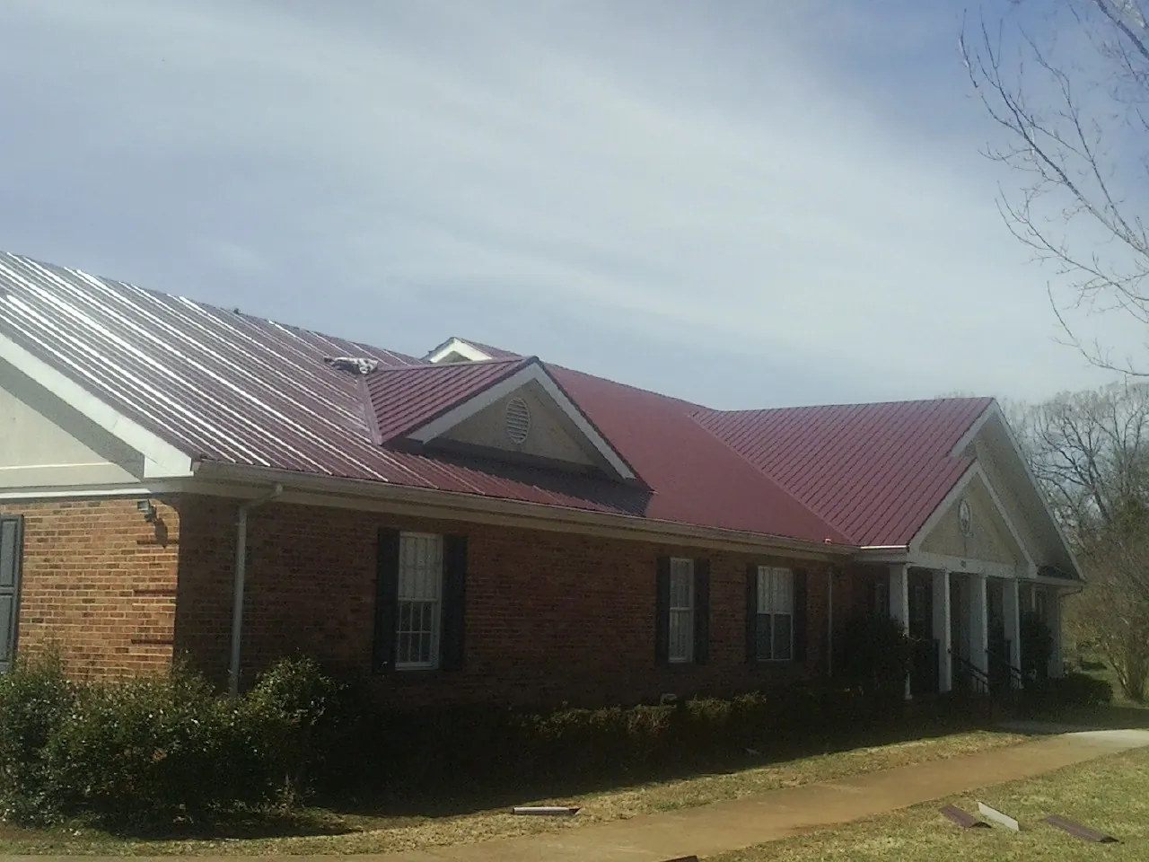 Red metal roof with gabled entries on a long brick building, from a Hail Damage Roof Repair job in Andrew