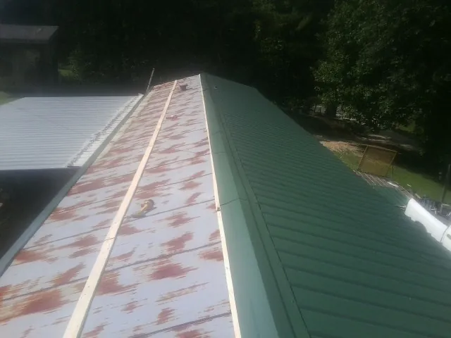 Old rusted panels beside newly installed green metal roofing — Wind Damage Roof Repair by Roofing Brothers in Andrew