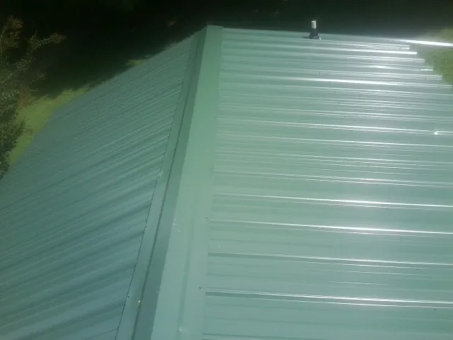 New green metal panels meeting at the ridge of a roof — Flat Roof Repair work by our crew in Andrew