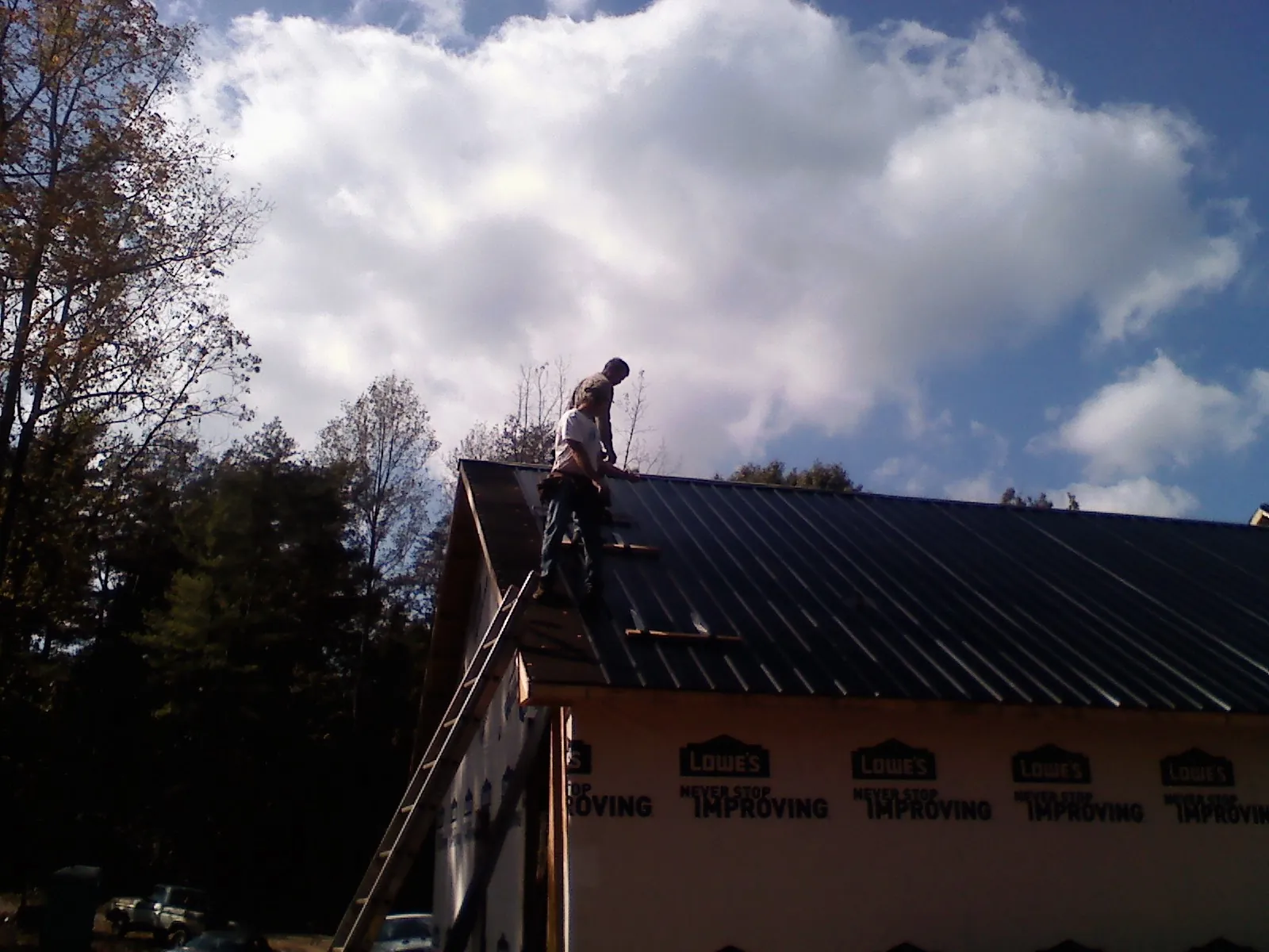 Roofer fastening dark metal panels high against a cloudy sky, from a Roof Inspection job in Andrew
