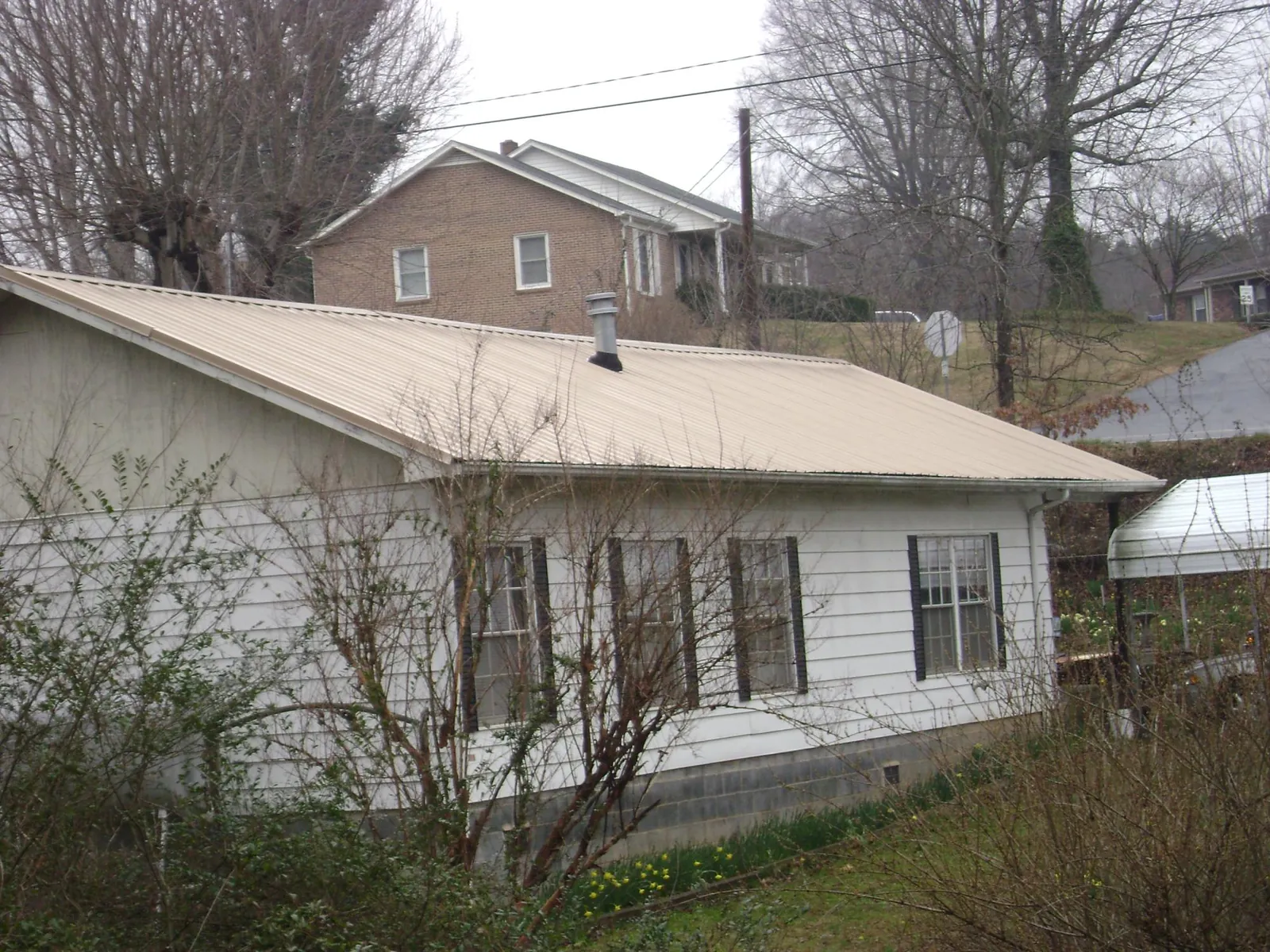 Tan metal roof on a white sided house set into a hillside — Commercial Roofing by Roofing Brothers in Andrew