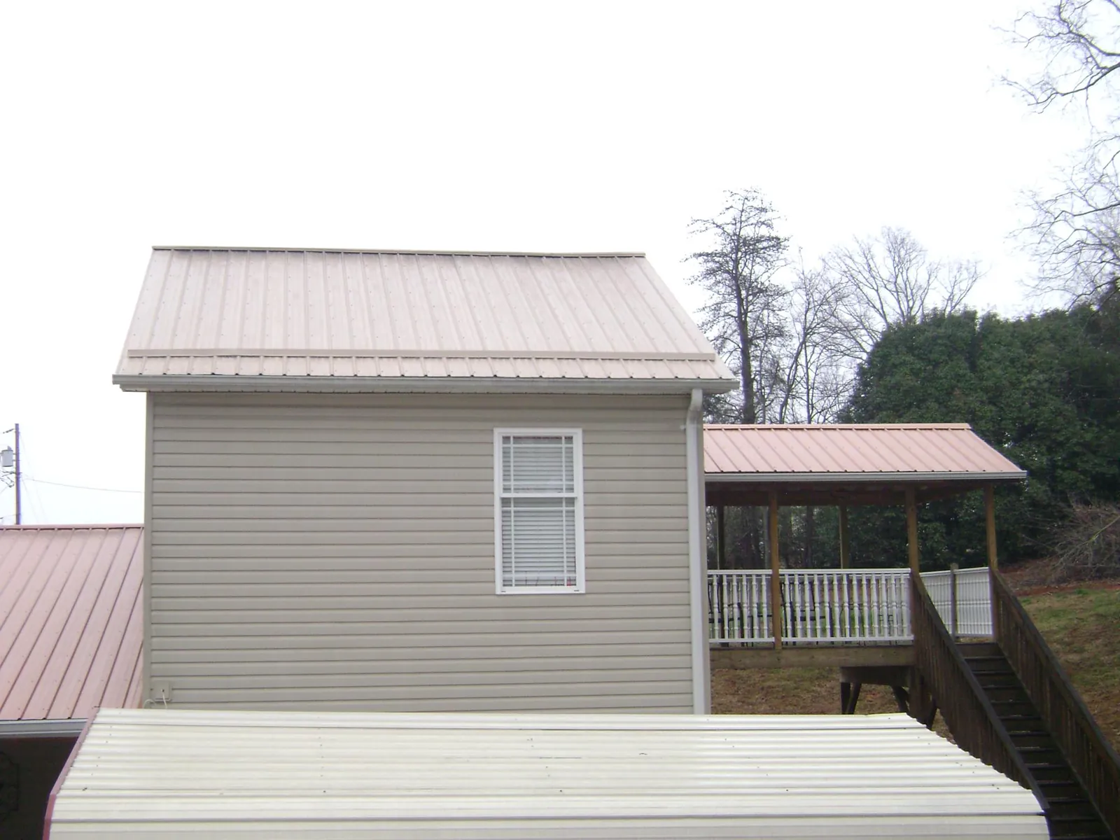 Tan metal roofs on a two story addition and attached porch, from a Roof Replacement job in Andrew